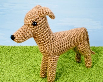 Puede incluir: Un juguete de perro de crochet marrón con ojos negros. El perro está de pie sobre una superficie verde.