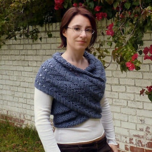 Peut inclure: Un châle crocheté bleu avec un col roulé et un design en forme de croix. Le châle est porté sur une chemise blanche à manches longues.