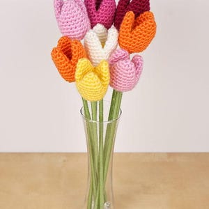 Op de afbeelding: Een boeket gehaakte tulpen in een glazen vaas. De tulpen zijn in tinten roze, oranje, geel en wit.