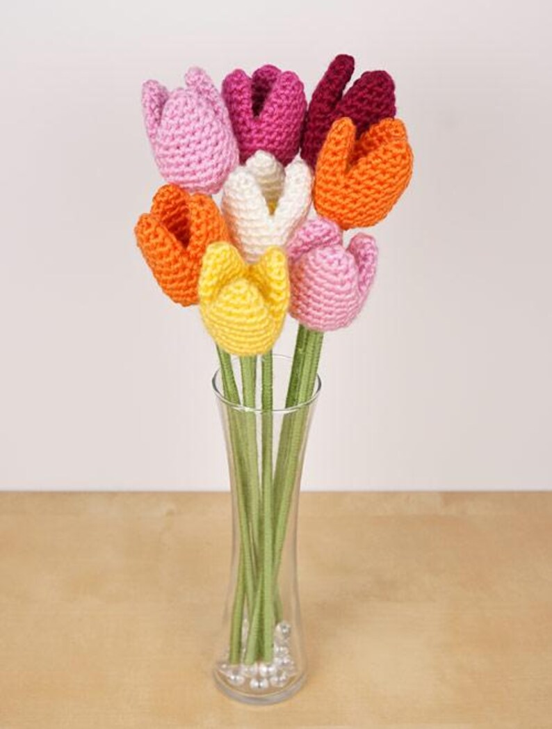 Op de afbeelding: Een boeket gehaakte tulpen in een glazen vaas. De tulpen zijn in tinten roze, oranje, geel en wit.