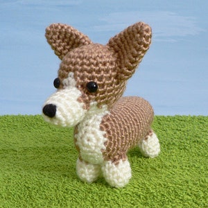 May include: A crocheted brown and white dog toy with black eyes. The toy is standing on a green surface.