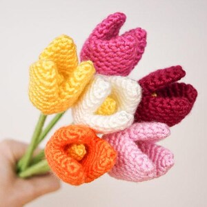 Op de afbeelding: Een boeket van zes gehaakte tulpen in verschillende kleuren, waaronder geel, wit, oranje, roze en rood.