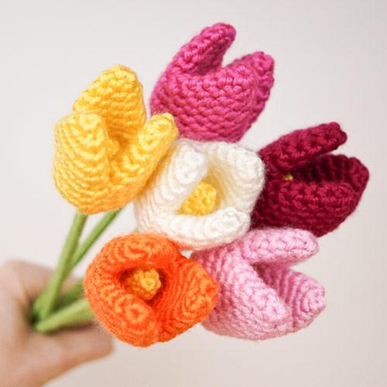 Op de afbeelding: Een boeket van zes gehaakte tulpen in verschillende kleuren, waaronder geel, wit, oranje, roze en rood.