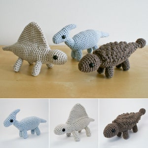 Può includere: Tre giocattoli di dinosauro all'uncinetto. Uno è uno stegosauro blu chiaro, uno è un ankylosaurus marrone e uno è uno spinosaurus beige.