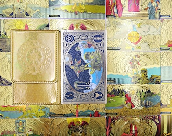 May include: A gold metallic card case with a circular embossed sun design sits next to a rectangular deck of tarot cards featuring a blue and silver border, a central illustration of a figure in a starry landscape, and various symbols.