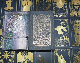May include: A holographic tarot card pouch with a circular geometric design and a black box featuring gold foil illustrations of The Fool tarot card and the text Gold foil Tarot, set against a background of various tarot card prints.