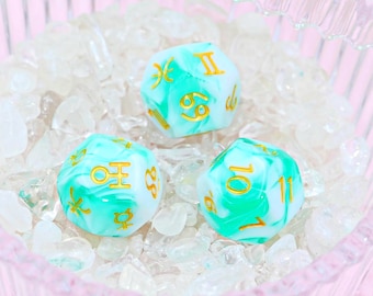 May include: Three teal and white marbled dice with gold zodiac symbols and numbers. The dice are sitting on a bed of white crystals.