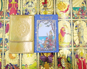 Puede incluir: Un estuche de almacenamiento rectangular de color dorado con un diseño circular en relieve junto a una caja de cartas de tarot azul con el texto "Waite Tarot deck" y "78 latest Waite Taro decks" con la ilustración de una figura junto al mar.