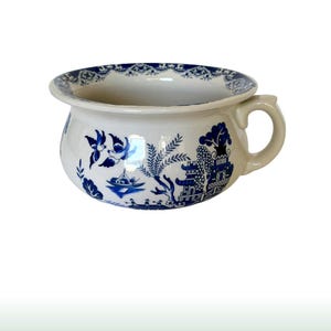 Puede incluir: Orinal de cerámica blanca con un diseño azul de patrón Willow. El orinal tiene forma redondeada, un asa y un borde decorativo. El patrón azul representa pájaros, barcos y pagodas.