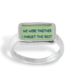 May include: A silver ring with a rectangular green enamel inlay. The inlay has the text "WE WERE TOGETHER I FORGET THE REST." in blue.