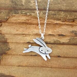 May include: A silver necklace featuring a small, detailed rabbit pendant. The rabbit is depicted in a running pose with its ears raised.