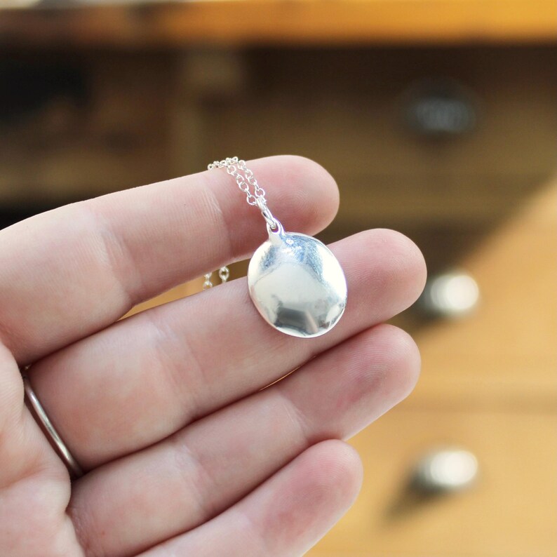 May include: A silver pendant necklace with a round, smooth, silver disc charm.