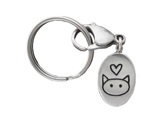 May include: Silver key chain with a small oval charm featuring a cartoon cat with a heart above it.