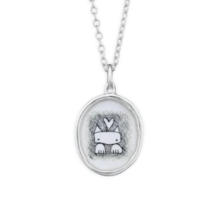 May include: A silver necklace with a round pendant featuring a black and white illustration of a cat with a heart on its head. The pendant is set against a white background with a black speckled texture.
