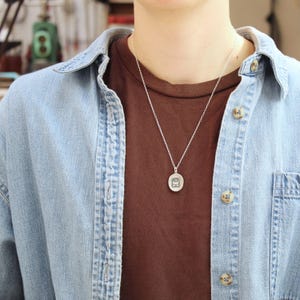 May include: A silver chain necklace with a small oval pendant featuring a geometric design.