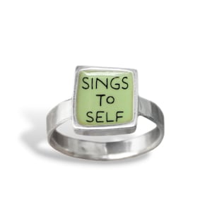 May include: A silver ring with a square green stone that says "SINGS TO SELF" in black lettering.
