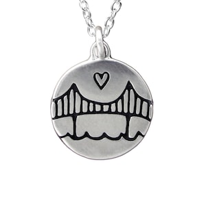 Simple line drawing of the Golden Gate Bridge with a water line and a heart above grace this round shaped pendant. Reversible with same image on both sides.