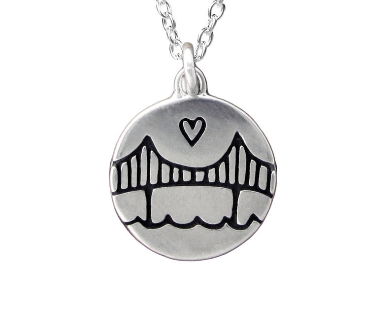 Simple line drawing of the Golden Gate Bridge with a water line and a heart above grace this round shaped pendant. Reversible with same image on both sides.