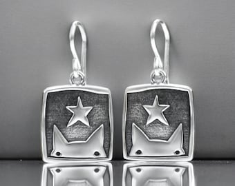 May include: A pair of silver dangle earrings with a square design featuring a cat's face and a star.