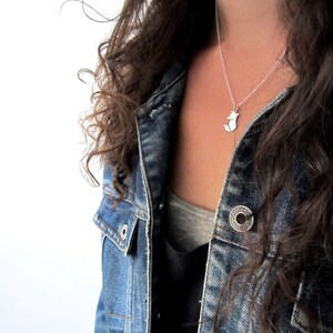 May include: A silver necklace with a small fox pendant. The necklace is worn by a person wearing a denim jacket.