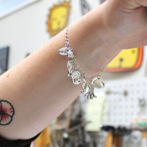 Puede incluir: Un brazalete de plata con varios dijes de criaturas marinas, incluyendo una medusa, un caballito de mar, un pez globo y un pulpo.
