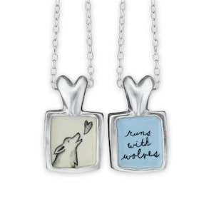 May include: Two silver necklaces with heart-shaped pendants. One pendant features a black and white illustration of a wolf howling at a heart, with the text "runs with wolves" on the other pendant.