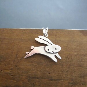 May include: A silver pendant necklace featuring a stylised rabbit design. The rabbit is depicted in a leaping pose with its ears raised.