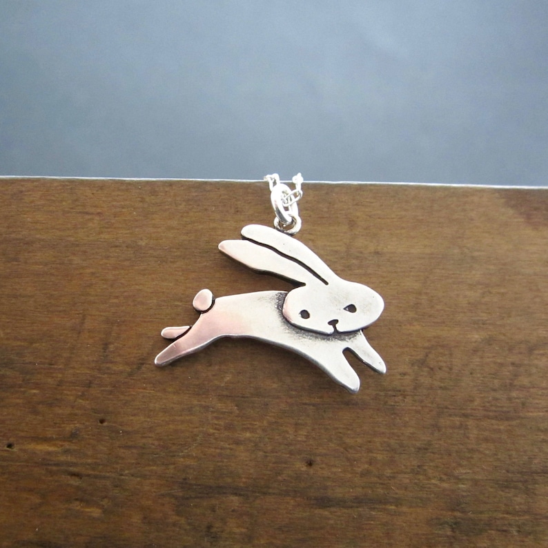 May include: A silver pendant necklace featuring a stylised rabbit design. The rabbit is depicted in a leaping pose with its ears raised.