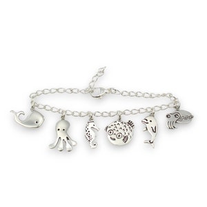 Puede incluir: Un brazalete de plata con una variedad de dijes de criaturas marinas, incluyendo una ballena, un pulpo, un caballito de mar, un pez globo, un delf&iacute;n y un cangrejo.