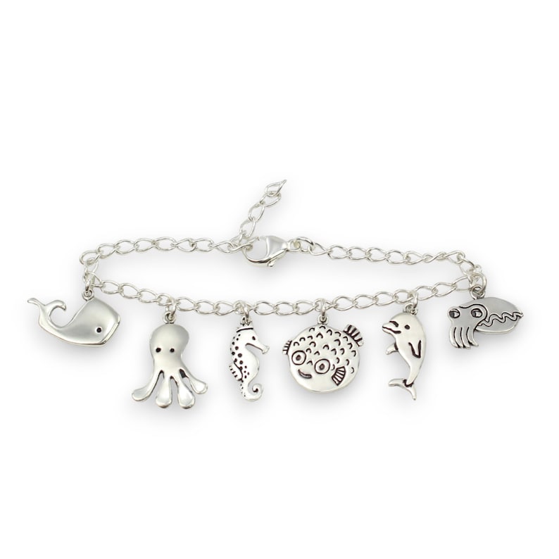 Puede incluir: Un brazalete de plata con una variedad de dijes de criaturas marinas, incluyendo una ballena, un pulpo, un caballito de mar, un pez globo, un delf&iacute;n y un cangrejo.