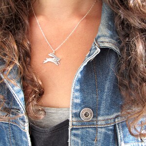 May include: A silver necklace featuring a small, stylised rabbit pendant. The necklace is worn by a person with long, brown hair and a denim jacket.