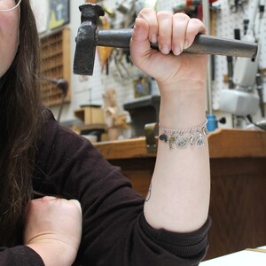 Puede incluir: Una persona lleva una camisa negra de manga larga con un brazalete de plata con varios encantos de criaturas marinas. El brazalete tiene una cadena de plata y encantos de un delf&iacute;n, un caballito de mar, un pulpo y una estrella de mar.