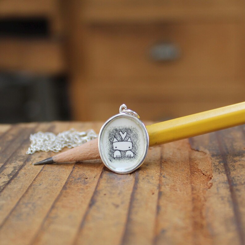 May include: A silver necklace with a round pendant featuring a black and white illustration of a cat with a heart above its head.