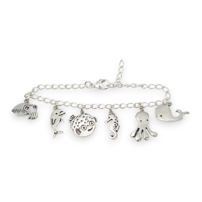 Puede incluir: Un brazalete de plata con una variedad de dijes de criaturas marinas, incluyendo un delf&iacute;n, un pez globo, un caballito de mar, un pulpo y una ballena.