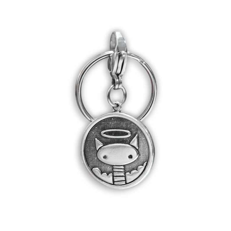 May include: Silver keyring with a round charm featuring a cartoon cat with a halo. The cat has a striped neck and is surrounded by clouds.
