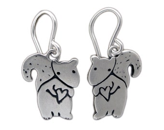 May include: A pair of silver-toned squirrel earrings. Each earring features a detailed squirrel design with a heart shape. The earrings have a hook closure and are set against a white background.