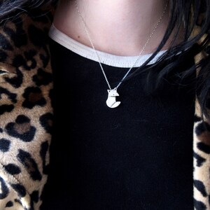 May include: A silver necklace with a fox pendant. The necklace is worn by a person wearing a black shirt and a leopard print jacket.
