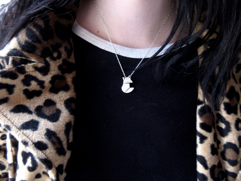 May include: A silver necklace with a fox pendant. The necklace is worn by a person wearing a black shirt and a leopard print jacket.