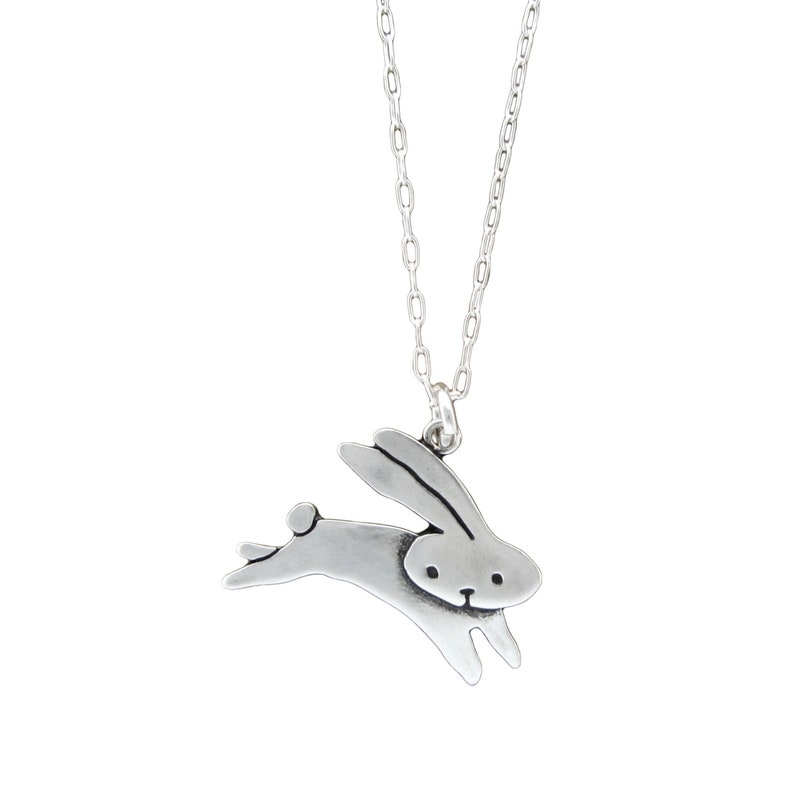 May include: A silver necklace featuring a simple, stylised bunny pendant. The bunny is depicted in a leaping pose with its ears up.