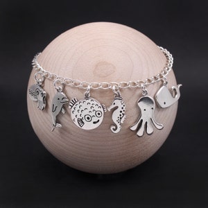 Puede incluir: Un brazalete de plata con varios dijes de criaturas marinas, incluyendo un delf&iacute;n, un pez globo, un caballito de mar, un pulpo y una ballena.