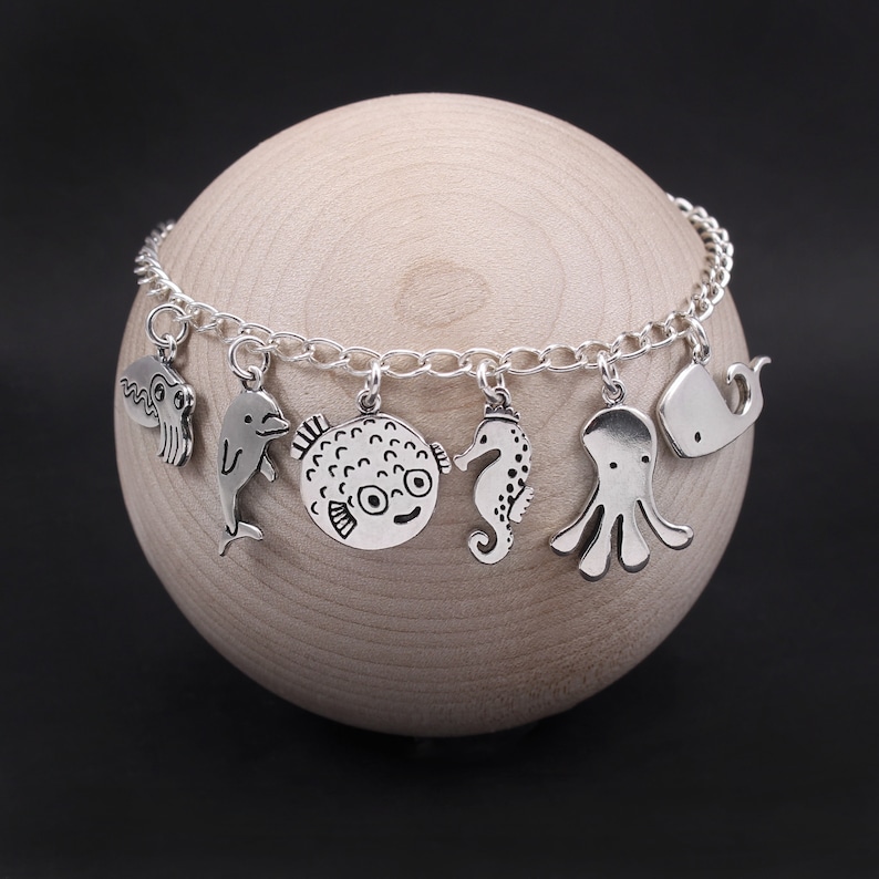 Puede incluir: Un brazalete de plata con varios dijes de criaturas marinas, incluyendo un delf&iacute;n, un pez globo, un caballito de mar, un pulpo y una ballena.