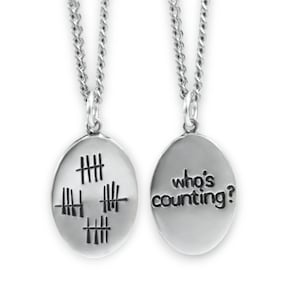 Könnte beinhalten: Eine silberne Halskette mit einem Anhänger, der auf der einen Seite Zählstriche und auf der anderen Seite den Text "who's counting?" trägt.