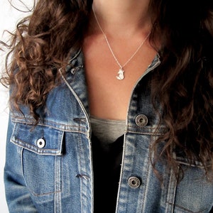 May include: A silver necklace with a small fox pendant. The necklace is worn by a person with long brown curly hair and a denim jacket.