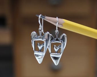 May include: Silver dangle earrings with a heart-shaped design. Each earring features a small heart inside a larger heart frame.