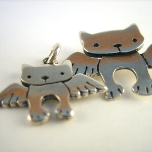 Puede incluir: Dos encantos de plata en forma de gatos con alas. El encanto m&aacute;s grande es ligeramente m&aacute;s grande que el encanto m&aacute;s peque&ntilde;o.
