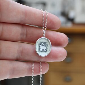 May include: A silver necklace with a round pendant featuring a black and white illustration of a cat with a heart on its head.