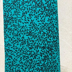 May include: Teal fabric with a black leaf pattern. The fabric is folded in half and the pattern is visible on both sides.