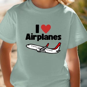 May include: A light blue t-shirt with a black and red graphic that says "I love airplanes" and a cartoon airplane.