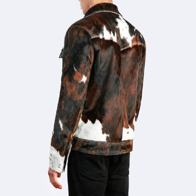 May include: A brown and white cowhide jacket with a zip closure. The jacket has a stand-up collar and long sleeves.