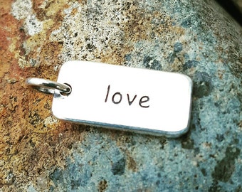 May include: Silver charm with the word "love" engraved on it.